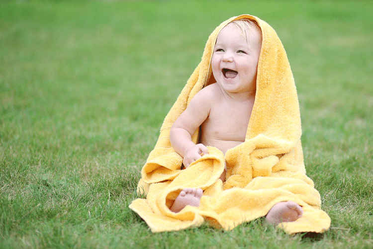 Happy baby wrapped in a yellow towel, sitting on grass!