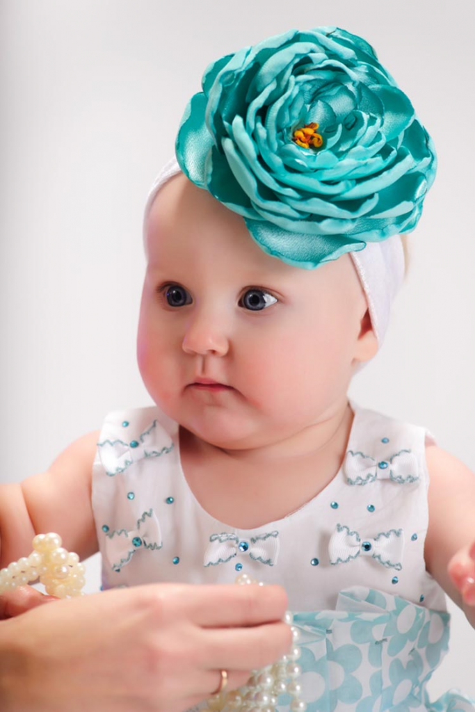 Infant with captivating beauty wearing a satin turquoise flower headgear and pearl jewellery!