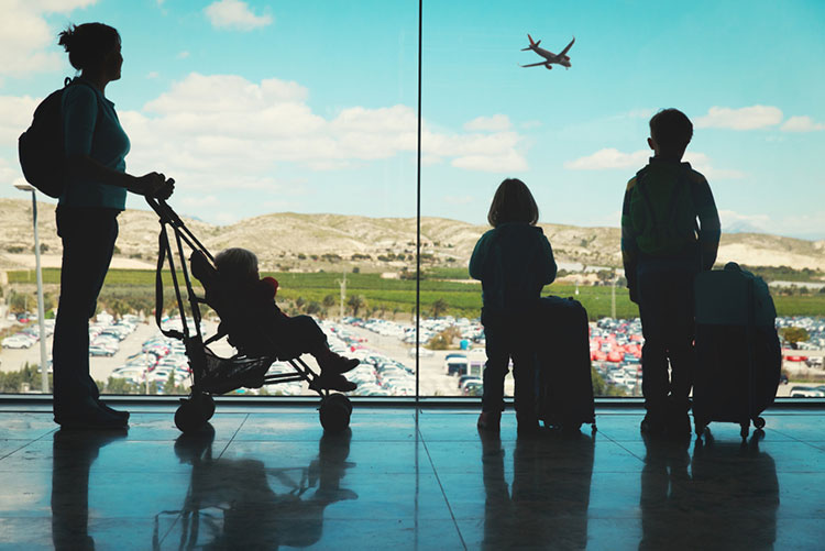 Silhouette of a family with bags standing in the airport looking at an airplane taking off