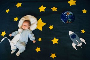 Baby sleeping on a bed spread with stars, earth, and rocket patterns