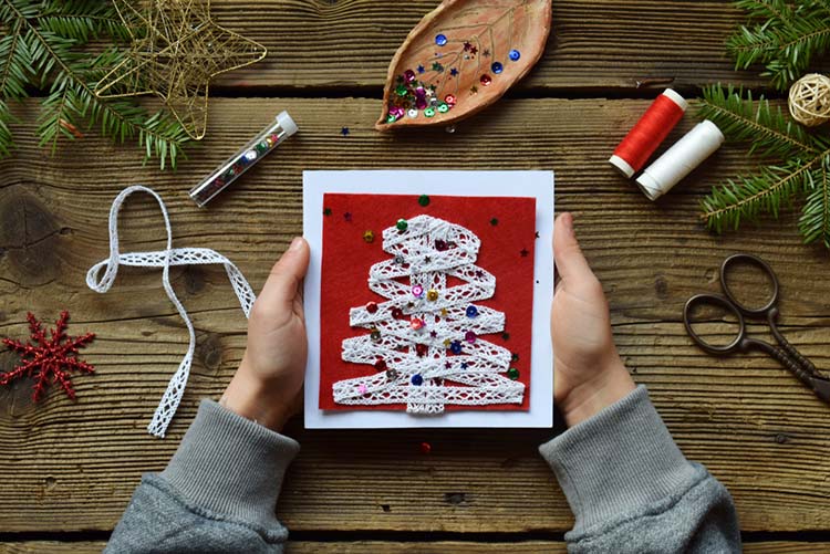 Hands holding a homemade Christmas card with supplies lying around