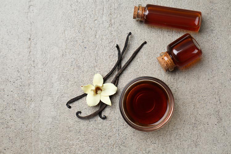 Vanilla essence in a bowl and 2 bottles with vanilla pods and a flower next to it