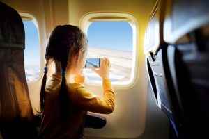 Girl taking a picture of the clouds from her window seat in side the plane