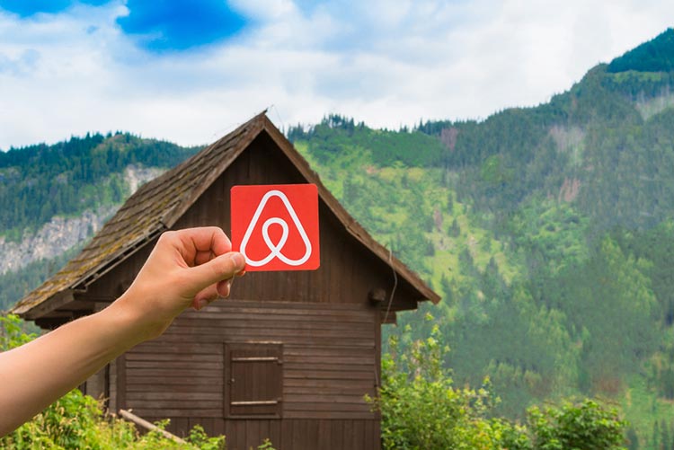 A person holding the logo of Airbnb in front of a cabin
