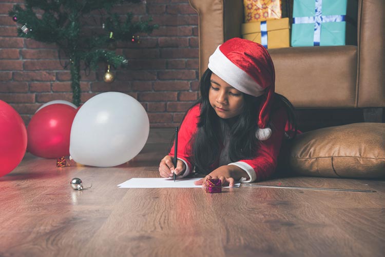 Girl lying on the floor wearing a Santa outfit and writing on a card