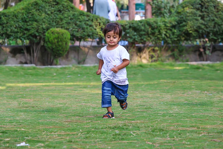 A baby boy running around in a park.