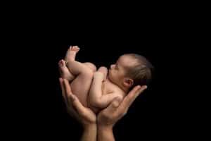 A newborn baby boy held in his parent's hands.