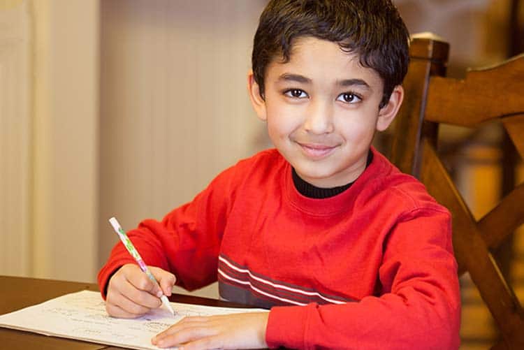 A young boy sitting at the table and writing.