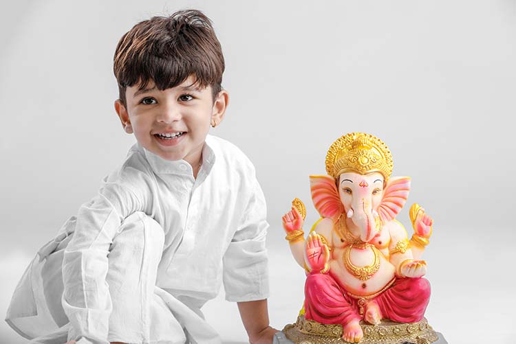 A young boy sitting next to an idol of Lord Ganesh.
