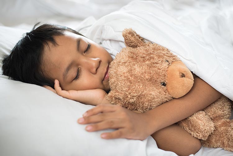 A young boy taking a nap with a teddy by his side.