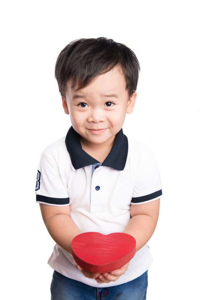 A cute little boy holding out a heart-shaped block.