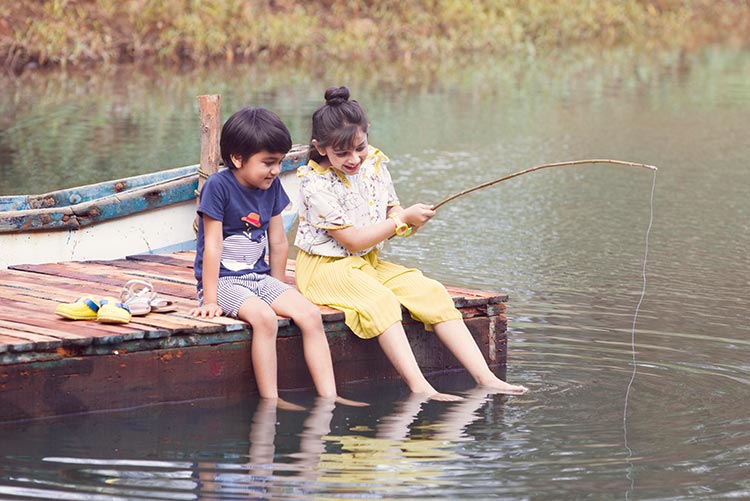 Boy and girl in co-ord sets fishing near the lake