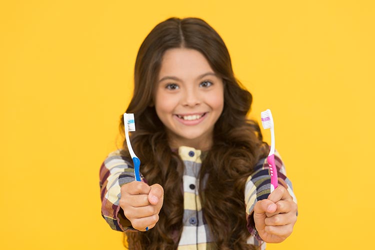 A girl holding out her tooth brushes.