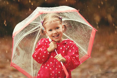 A young girl smiles as she holds an umbrella in the rain.
