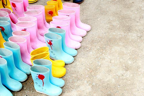 A row of colourful rain boots arranged on two stairs.