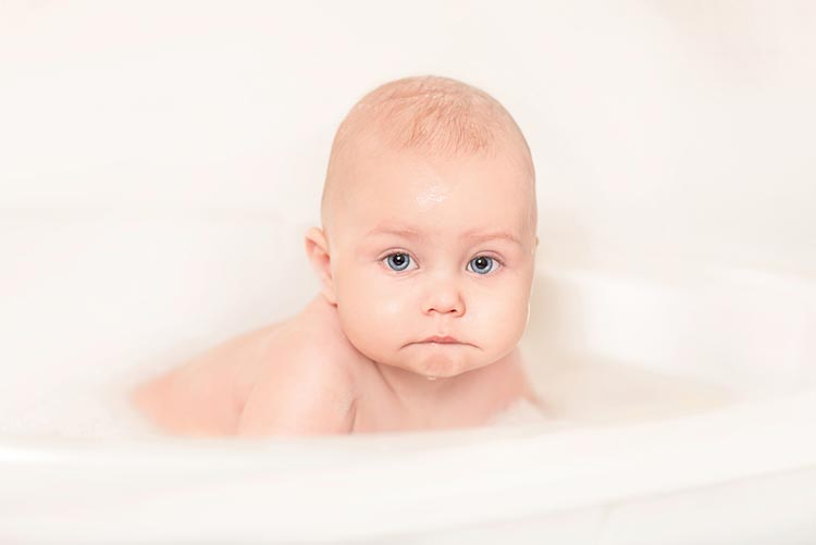 Adorable infant sitting in a bathtub.
