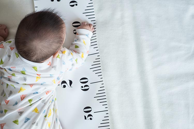 A baby boy crawling on a gigantic measuring tape.