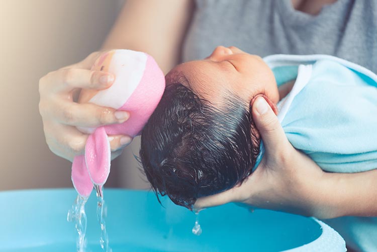 A mother using a baby sponge for her baby's head.