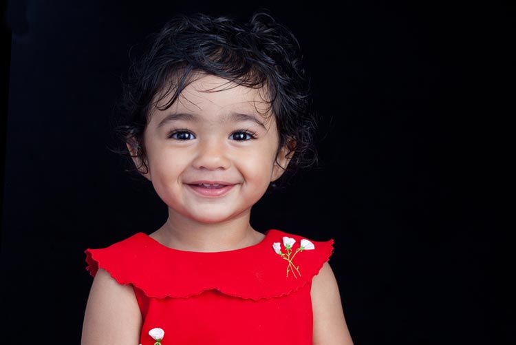 Portrait of a smiling toddler standing against a black backdrop.