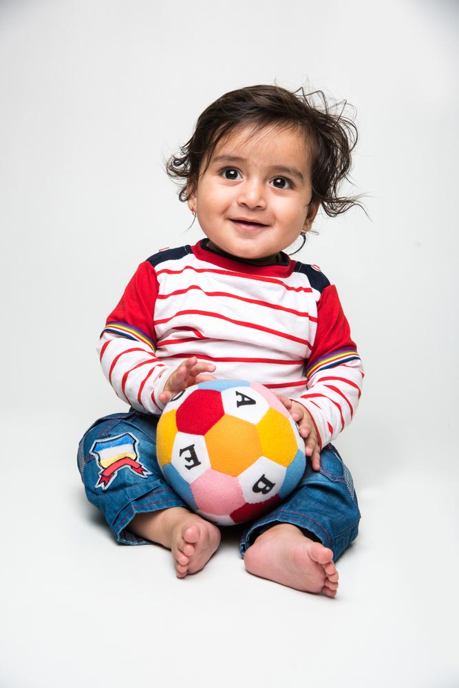 Toddler sitting with a ball on his lap.