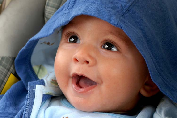 Excited toddler sitting with his hoodie up in his stroller.