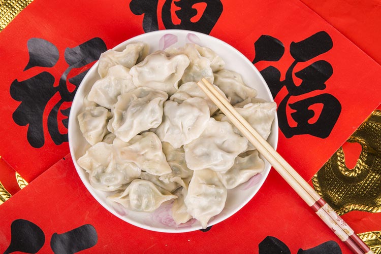 Chinese New Year lucky food - Jiaozi or dumplings served on a white plate with chopsticks.
