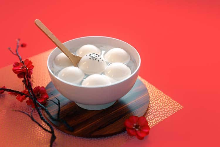 Sweet rice balls - a Chinese New Year traditional food item served in a white bowl placed on a wooden coaster.