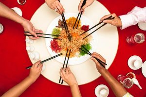 Multiple hands holding chopsticks and eating Yee Sang during the Chinese New Year.