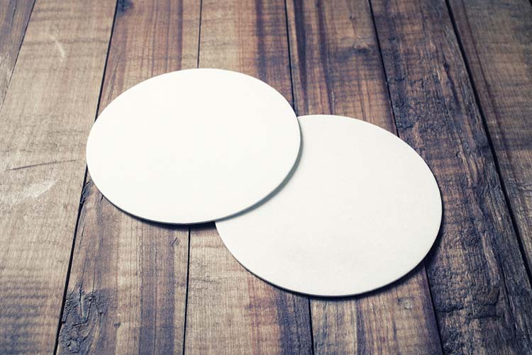 Two white coasters kept on a wooden table.