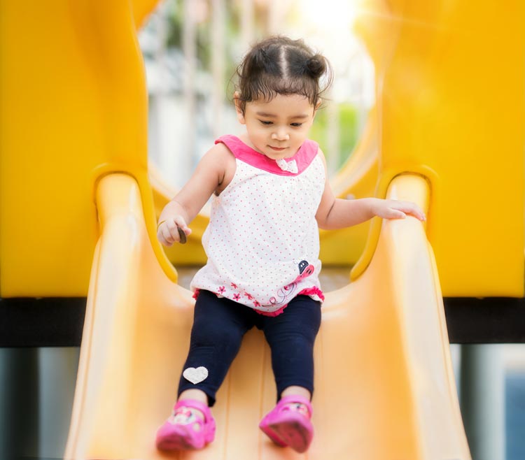 Adorable young girl coming down a slide in a playground.