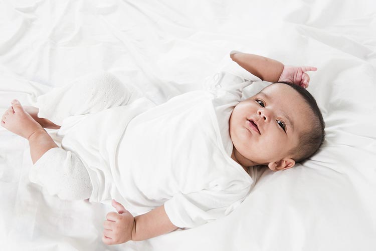 Portrait of an adorable infant in white lying on the bed.