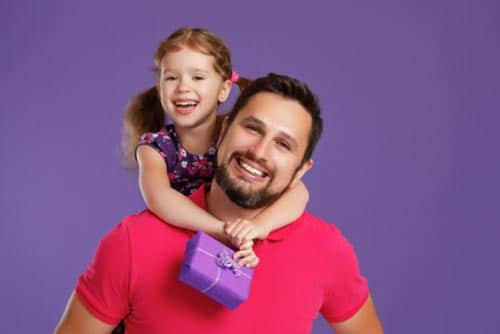 A dad carries his daughter while she holds a tiny present in her hands.
