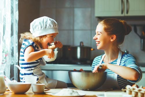 A mother smiles as she watches her daughter eat the cake dough.