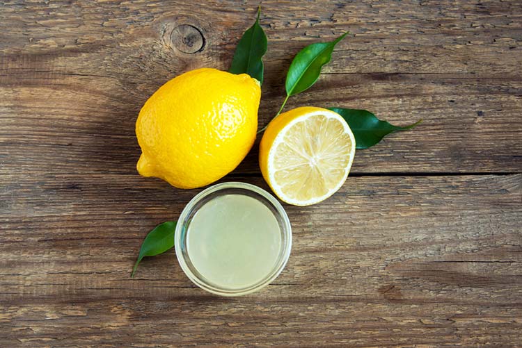 Freshly squeezed lemon juice kept on a wooden table along with lemons.