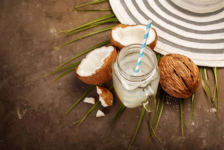 Agua de coco servida con pajita y con cocos guardados a un lado.