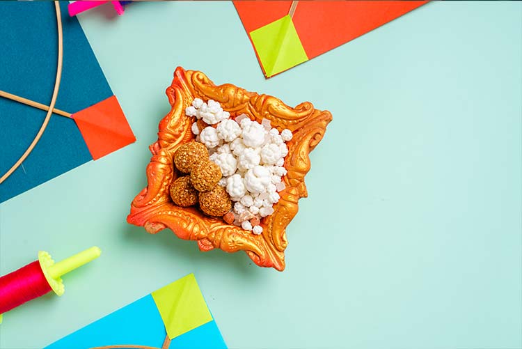 Ladoos and sugar placed in a bowl around colourful kites.