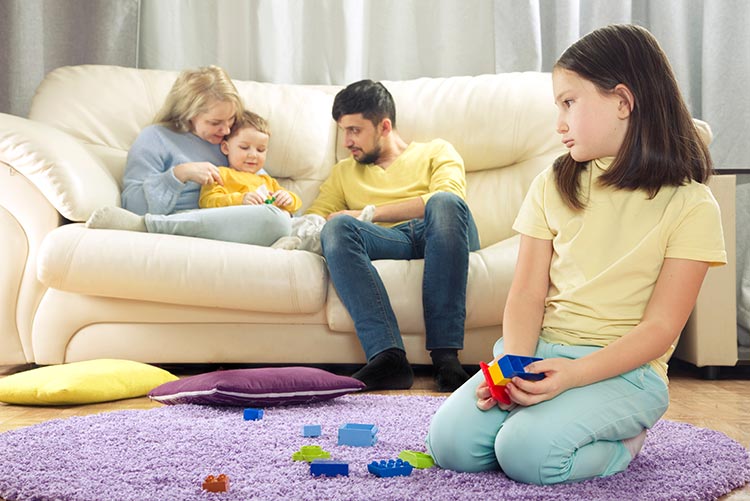 A middle child feeling sad as she watches her parents play with the baby.