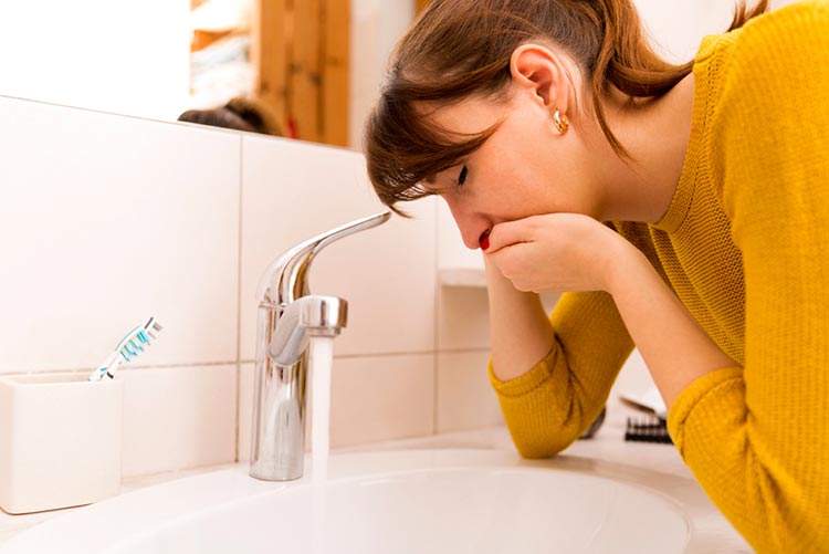 Nauseous woman bending over the sink