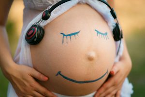 Closeup of a pregnant belly with a smiling face listening to music drawn on it.