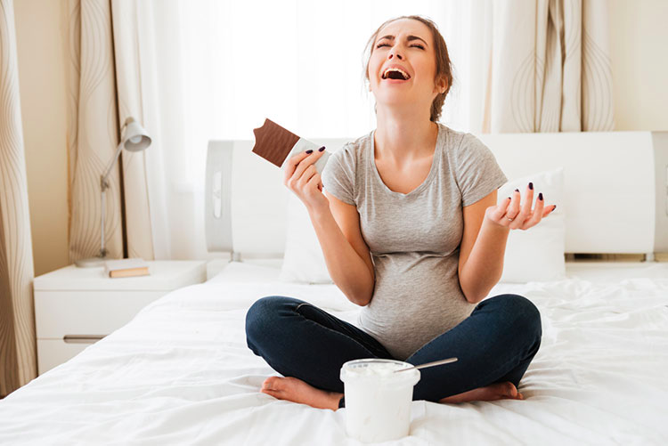 Stressed out pregnant woman sitting on the bed, eating chocolate!