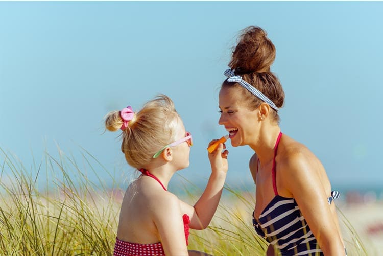 Daughter applying lip balm on her mother’s lips at the beach