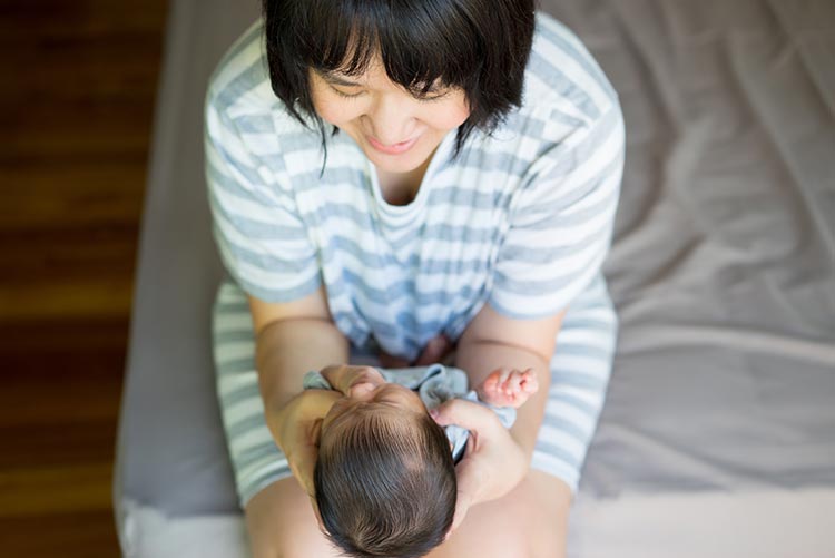 A mother holding her newborn by his head and supporting the neck.