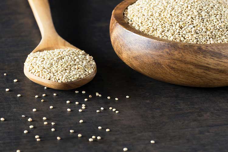 White quinoa seeds on a wooden spoon and bowl.