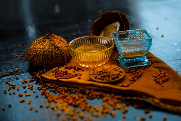 Dana methi or fenugreek seeds with coconut oil in a glass bowl placed on a wooden surface.