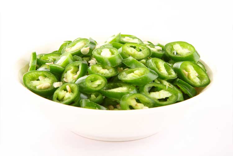 Chopped green chillies kept in a white glass bowl.