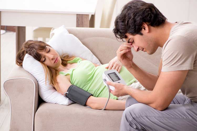 Husband checking his pregnant wife’s blood pressure using a machine.