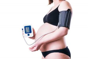 Pregnant woman measuring her blood pressure on a machine.