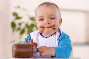 A baby boy enjoying a jar of chocolate.