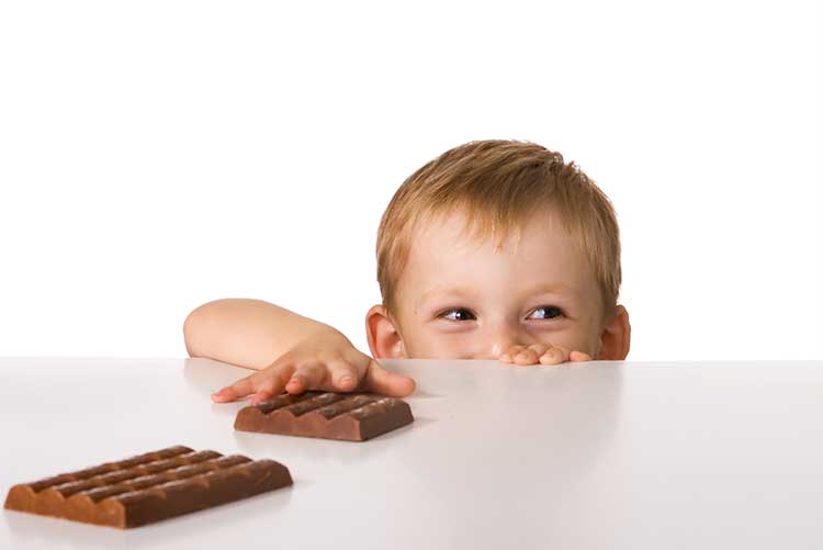 A young boy slyly reaching out for a bar of chocolate.