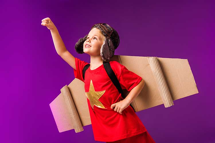 A young boy pretends to fly wearing a pair of cardboard wings.